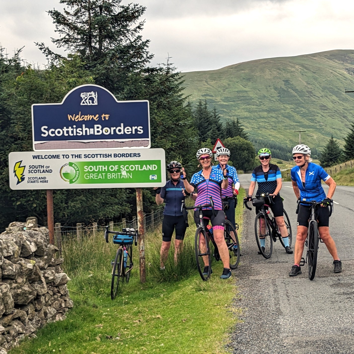 A group of cyclists next to a sign Wecome to the Scottish Borders Borders set in beautiful countryside